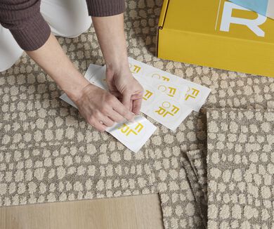Hands of a person using a FLORdot to assemble a FLOR area rug from carpet tiles.
